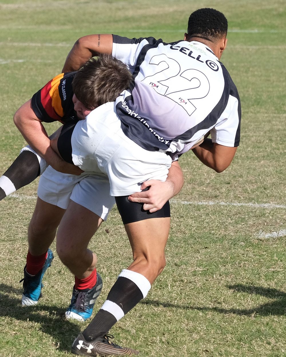 Un jugador taclea a la altura de la cadera, con la cabeza a un lado del rival y los brazos cerrando alrededor de sus piernas